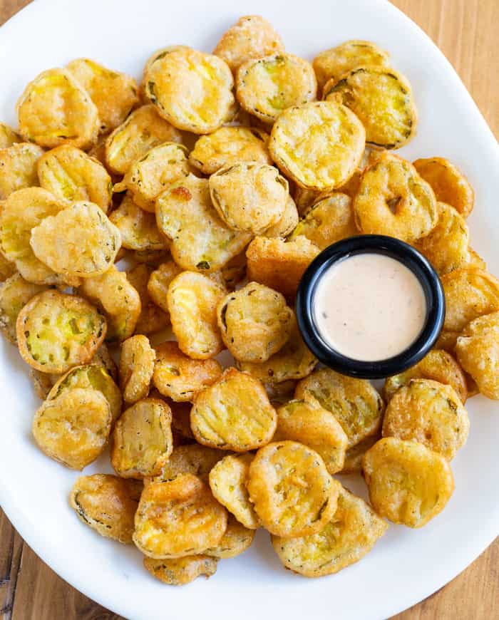 An overhead view of an oval white plate full of fried pickles and a black ramekin of dipping sauce.