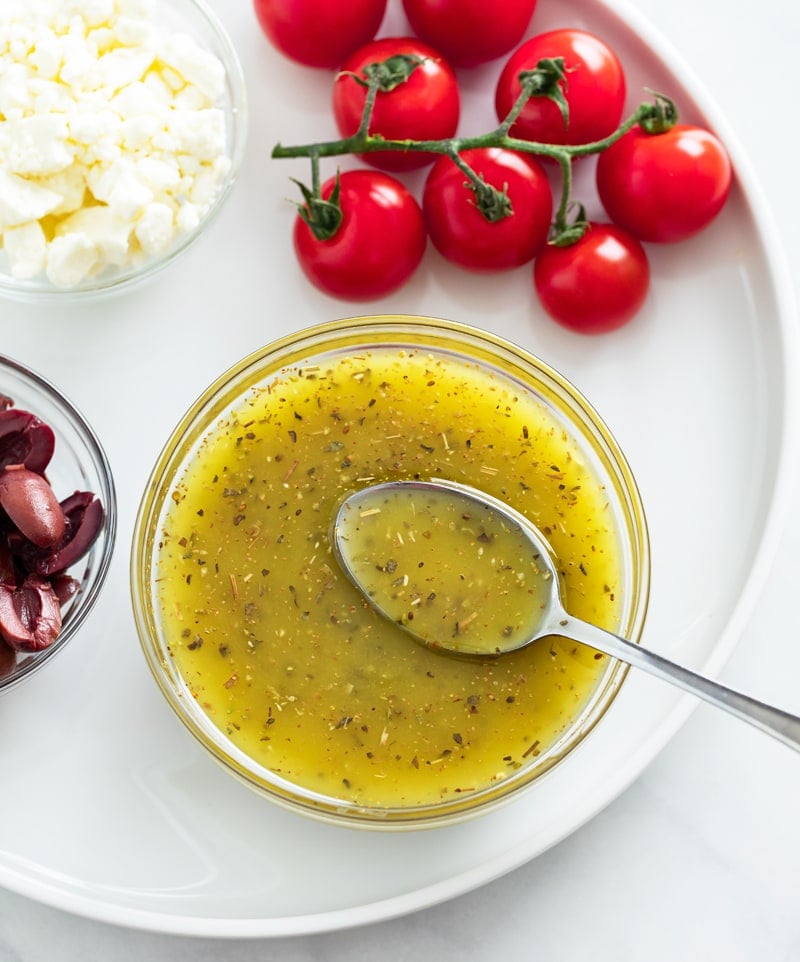 Overhead view of a glass cup filled with Greek Salad Dressing with a spoon in it.