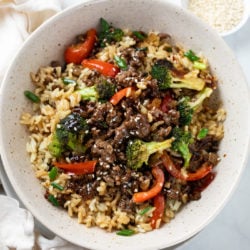 A bowl of ground beef and broccoli over rice with bell peppers.