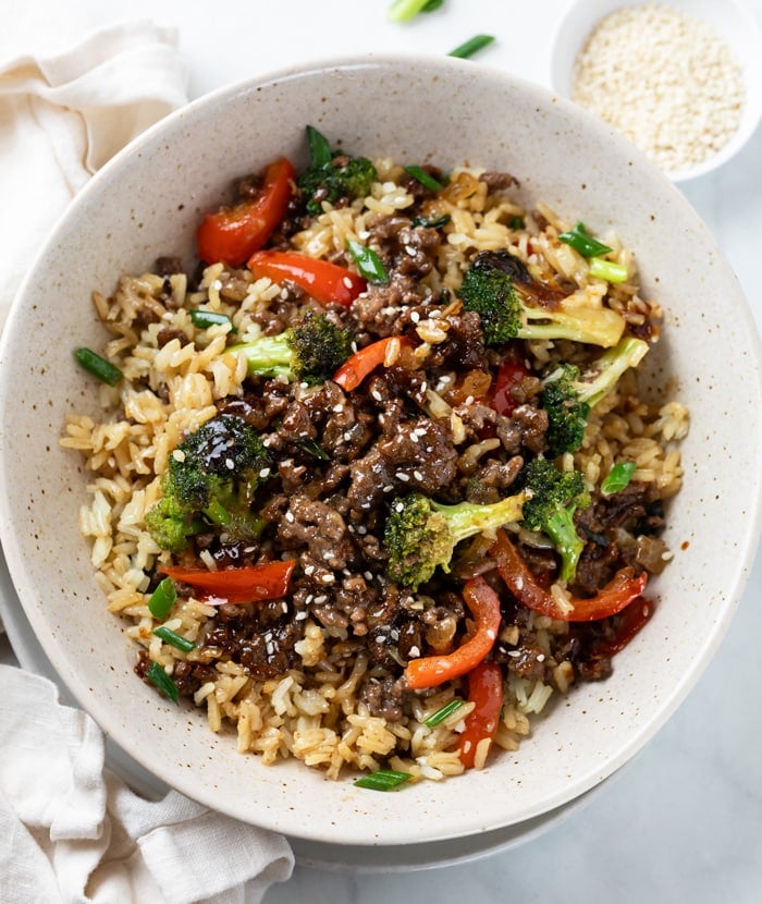 A bowl of ground beef and broccoli over rice with bell peppers.