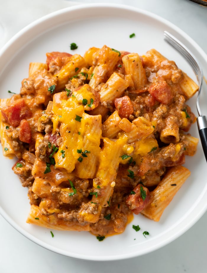 A white plate with ground beef casserole topped with fresh parsley and a fork on other side.