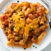 Ground Beef Casserole on a white plate topped with melted cheese.