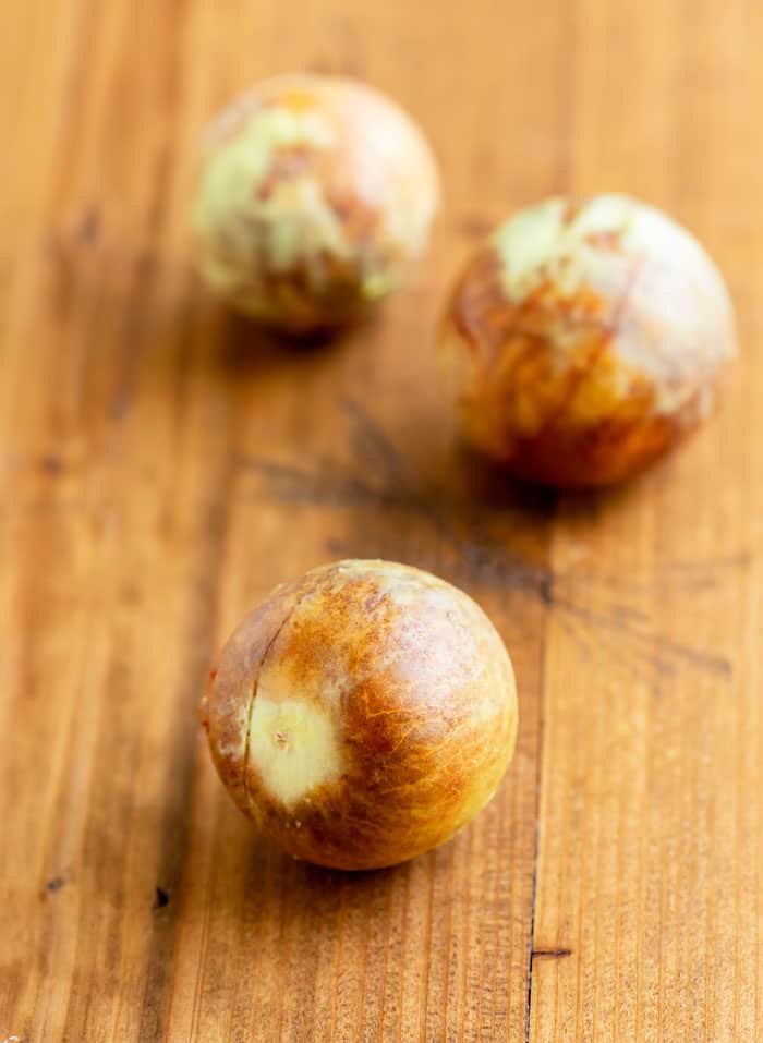 3 avocado pits on a wooden surface.