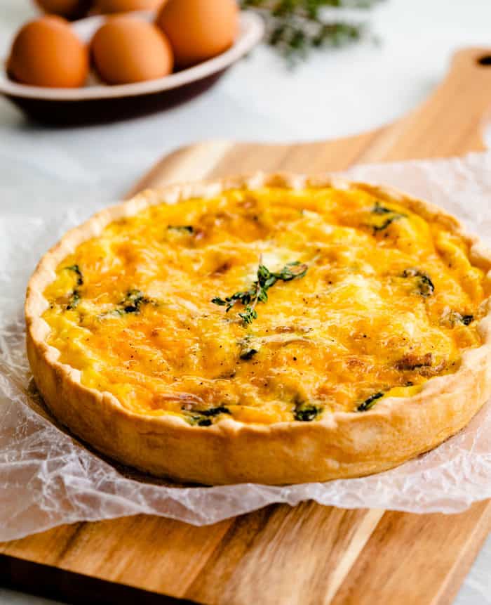 Ham and cheese quiche topped with rosemary on a wooden cutting board.