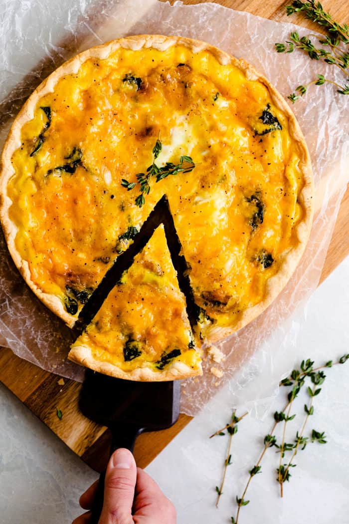 overhead view of a ham and cheese quiche topped with fresh rosemary with a slice being pulled out.