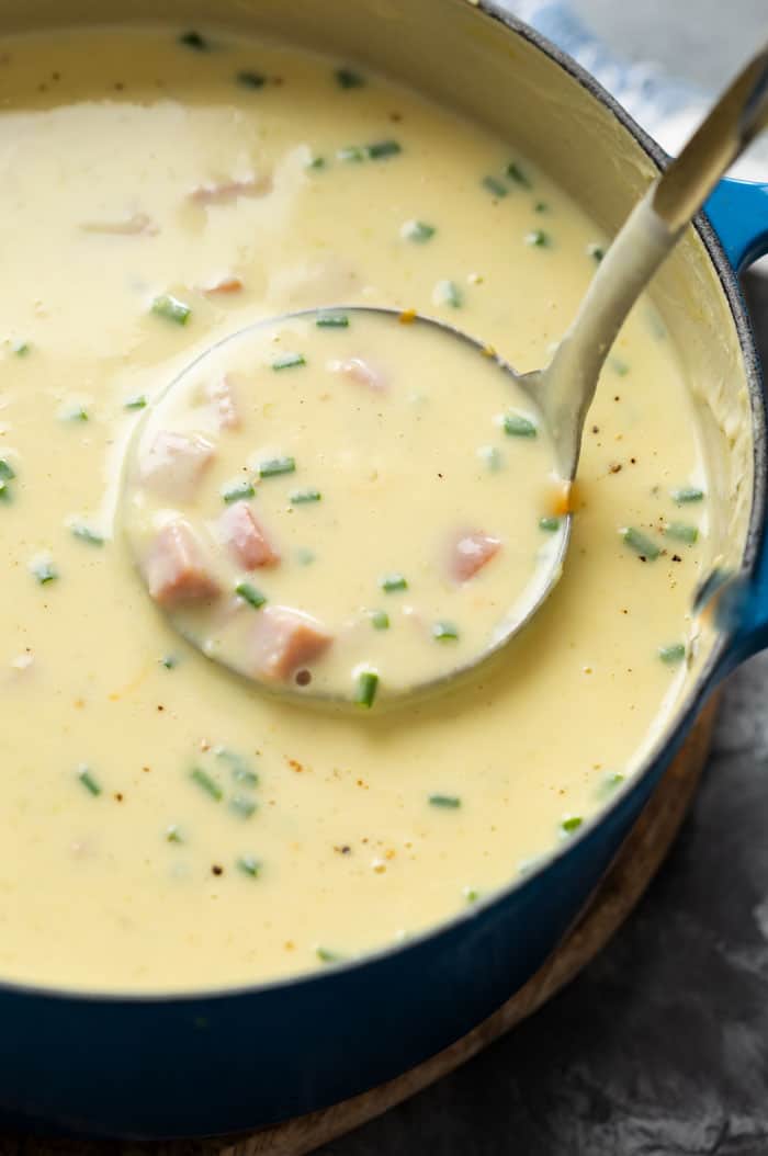 A soup ladle scooping up ham and potato soup from a soup pot.