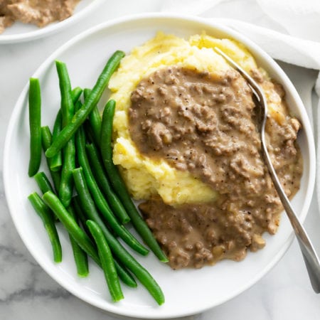 A pile of potatoes topped with Hamburger Gravy on a plate with green beans.