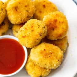 A plate of golden chicken nuggets on a white plate with sweet and sour sauce.