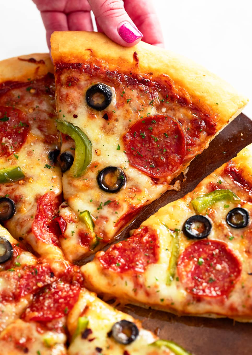 A hand pulling up a slice of homemade pizza from a pizza pan.