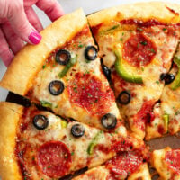 A hand pulling up a slice of homemade pizza with a golden crust and toppings.