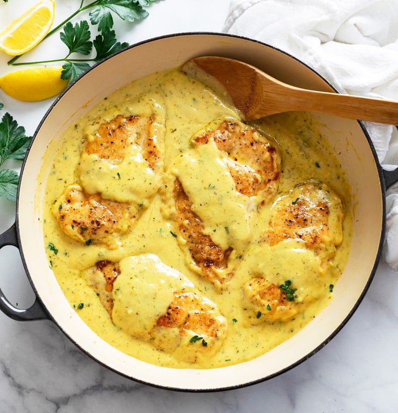 A skillet filled with Honey Mustard Chicken with a wooden spoon in it.