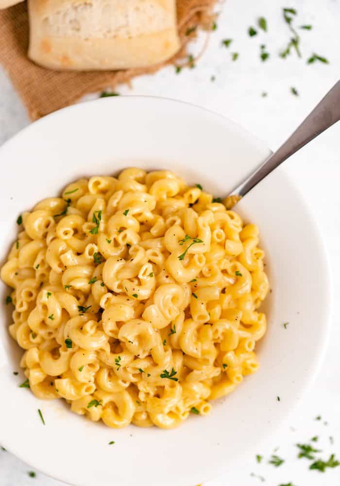 A bowl of macaroni and cheese with chopped parsley sprinkled on top and around the bowl.