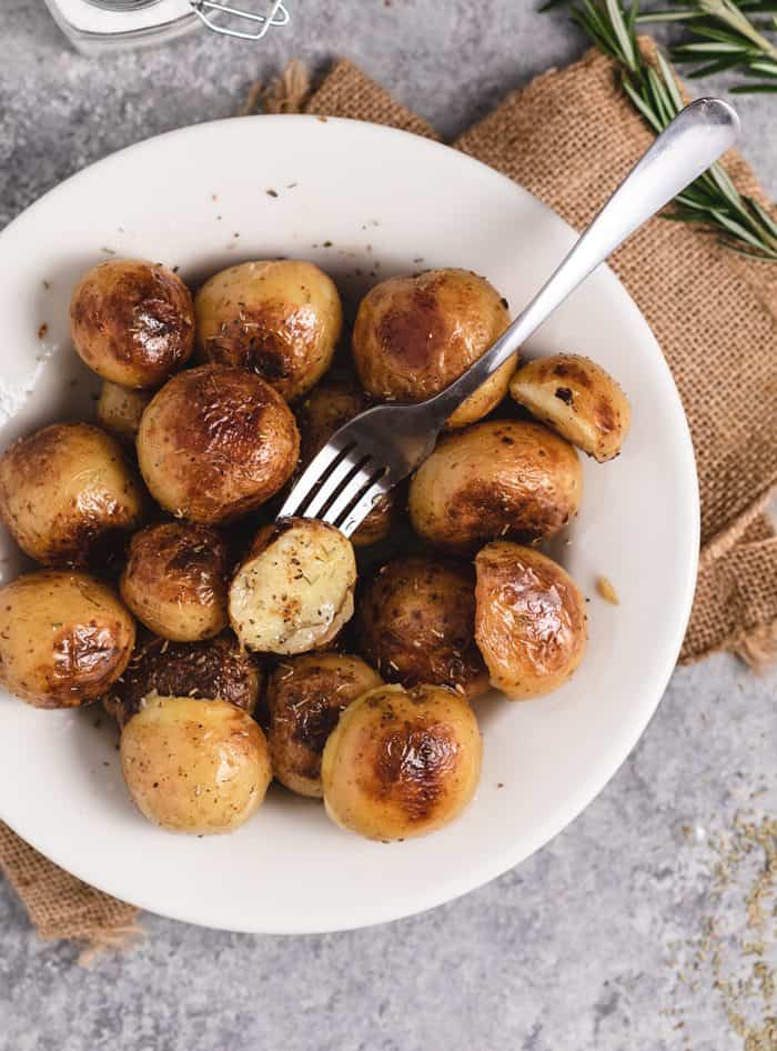 A white plate with roasted potatoes and a fork holding one that's been cut in half.