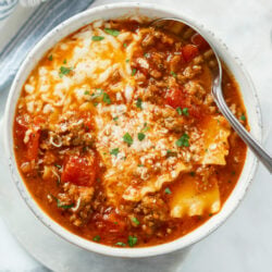 Lasagna Soup in a white bowl with cheese on top and a spoon on the side.