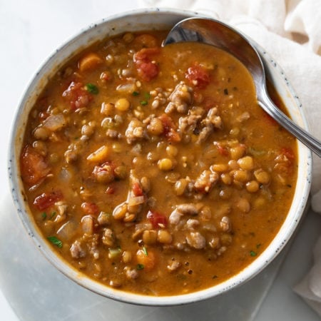 A bowl of Lentil Sausage Soup with a spoon on the side.