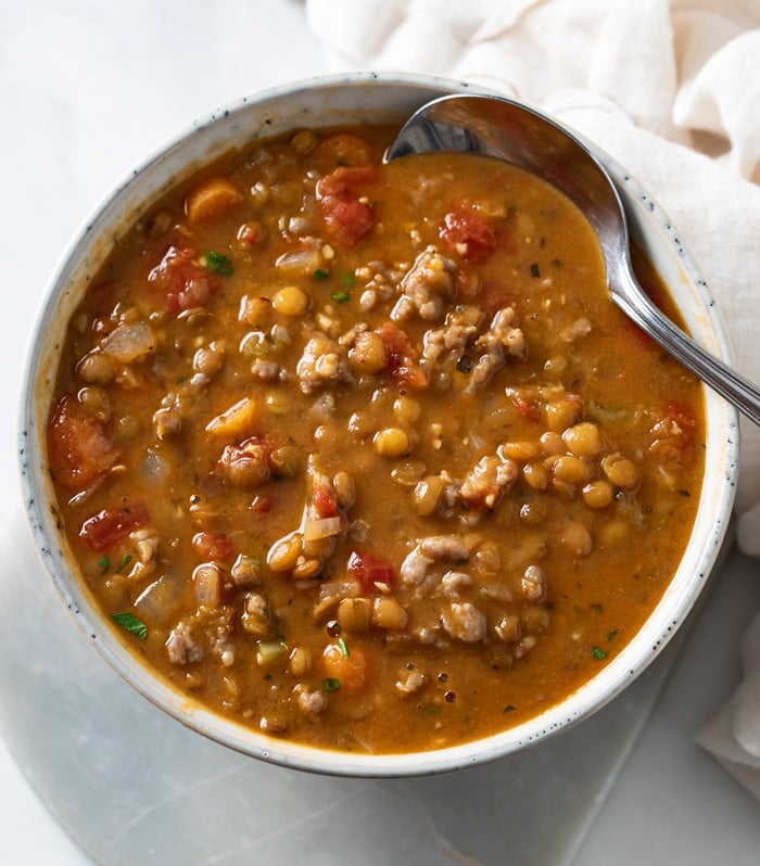 A bowl of Lentil Sausage Soup with a spoon on the side.