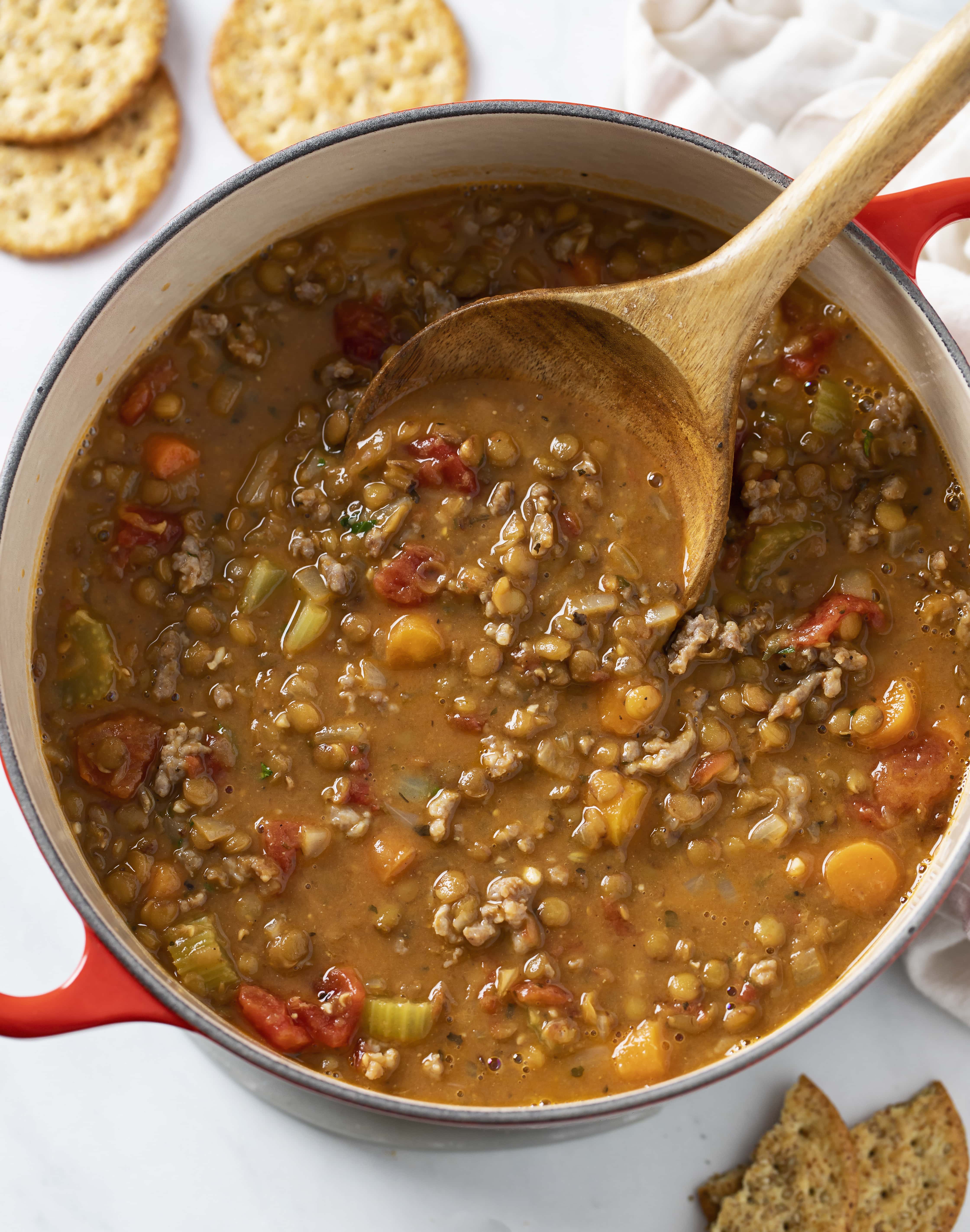 A red Dutch oven filled with Lentil Sausage Soup with a wooden spoon in it.