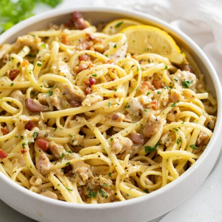 A white bowl of Linguine with Clams with lemon wedges on the side.