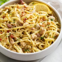 Linguine with Clams in a white wine sauce in a white bowl with lemon wedges.