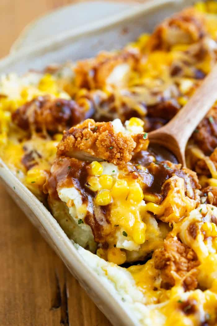 Close up shot of a wooden spoon scooping out mashed potato casserole with crispy chicken.