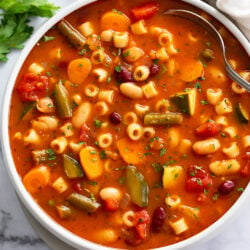 Minestrone Soup in a white bowl with a spoon on the side.