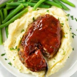 Mini Meatloaf topped with glaze on a pile of mashed potatoes with green beans.