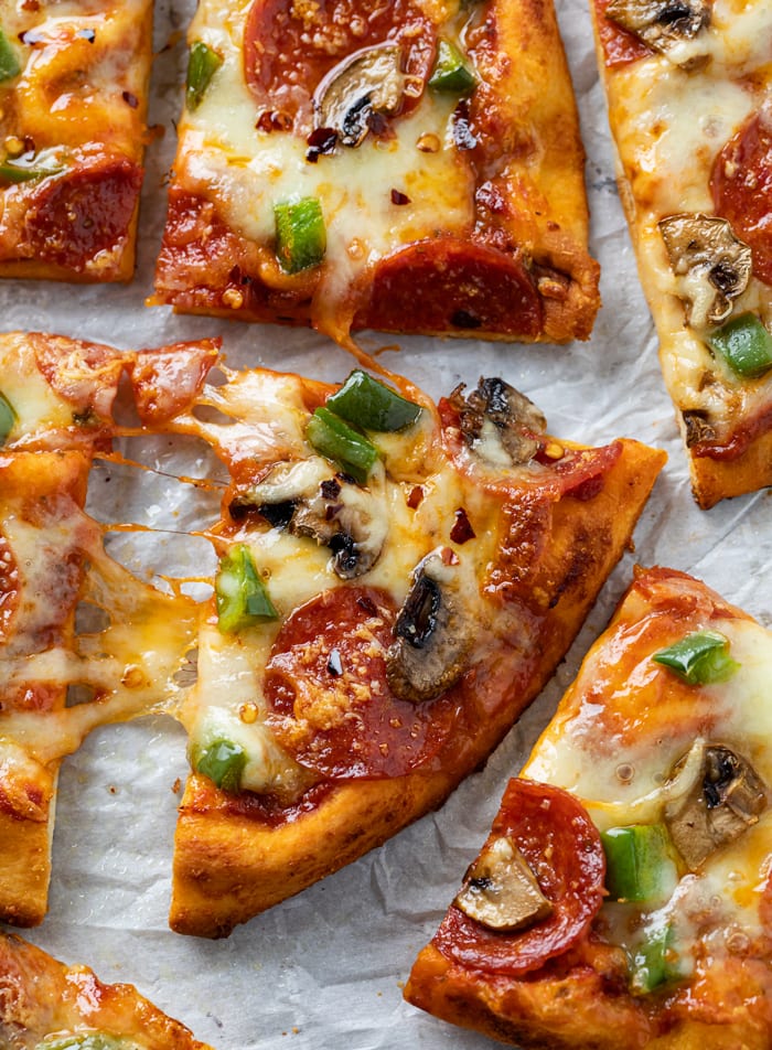 A slice of Naan Pizza with mushrooms, pepperoni, and peppers.