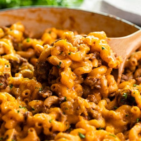 A skillet with a wooden spoon scooping up Cheeseburger Casserole