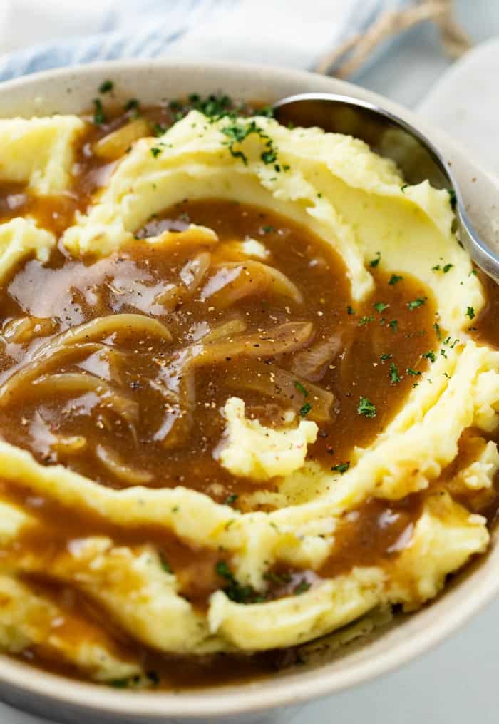 A bowl of creamy mashed potatoes topped with brown onion gravy.