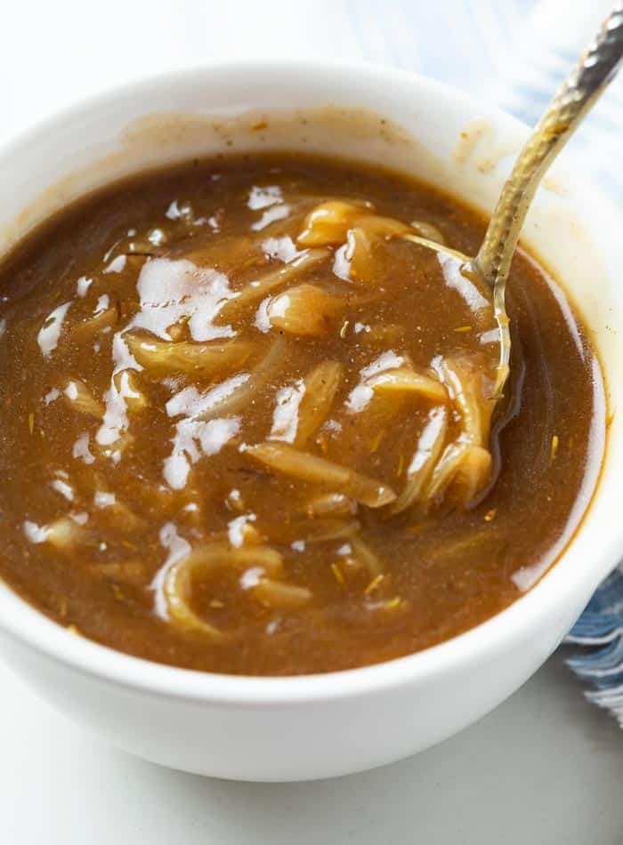 A white bowl with a ladle scooping out brown onion gravy from it.