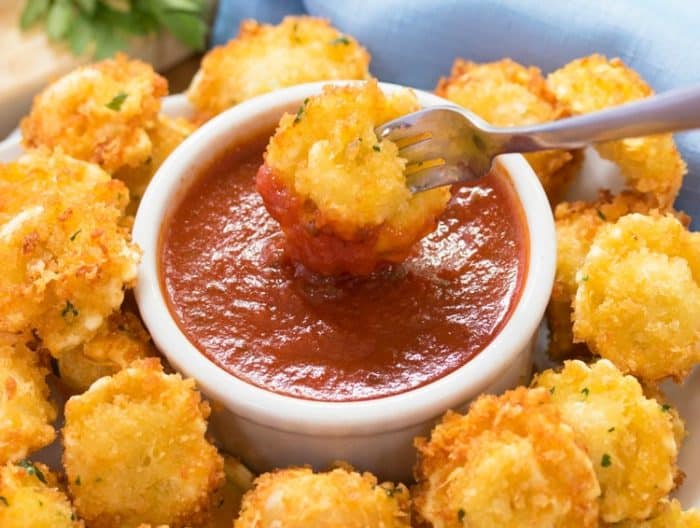 Fried tortellini on a fork being dipped into a ramekin of marinara sauce.