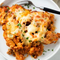 A white plate with penne in a meat sauce topped with cheese and fresh parsley.