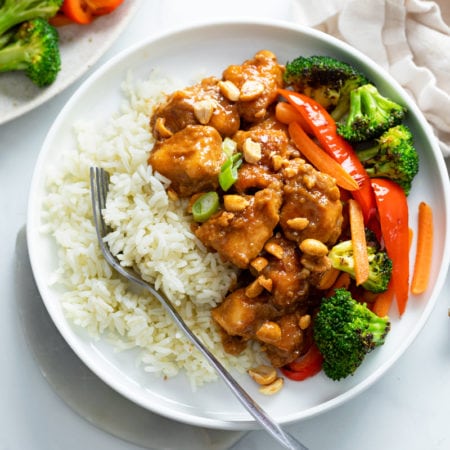 A white plate with rice and peanut butter chicken with stir-fried vegetables.