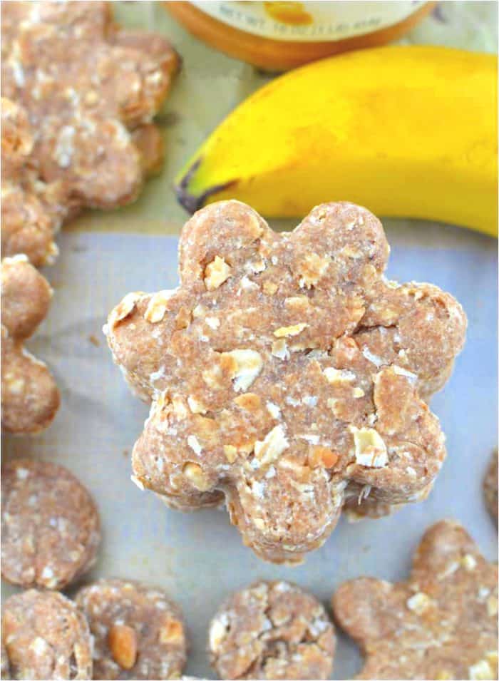 homemade dog treats stacked up on a white surface next to other treats and banana.