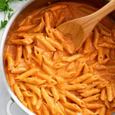 A skillet filled with Pink Sauce Pasta with a wooden spoon.