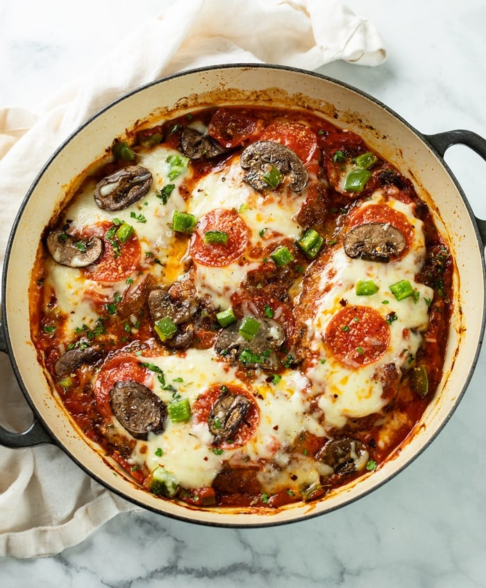 A round skillet filled with Pizza Chicken with mozzarella cheese and pizza toppings.