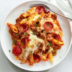 A white plate of Pizza Pasta with Pepperoni and meat sauce.