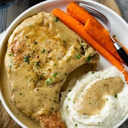 A white plate with Pork Chops in Gravy with carrots and mashed potatoes.