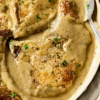 Seared Pork Chops in a skillet smothered with brown gravy with parsley on top.