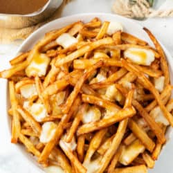 A white plate full of homemade poutine with french fries, gravy, and melted cheese curds.