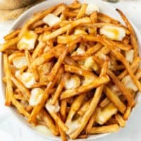 A plate piled with homemade poutine with brown gravy and melted cheese curds.