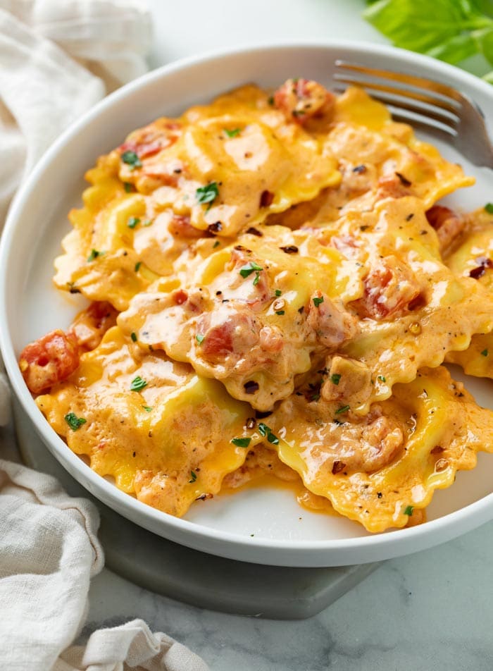 A white plate with Ravioli in a tomato cream sauce with tomatoes.