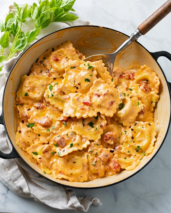 A pot of Ravioli in a cream sauce with tomatoes.