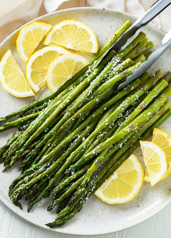 Kitchen tongs picking up a stack of Roasted Asparagus topped with grated Parmesan Cheese. 