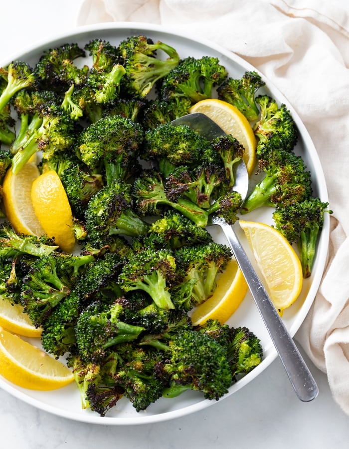 A white plate with roasted broccoli and slices of lemon with a spoon.