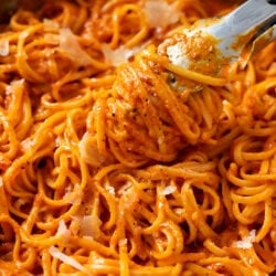 Kitchen Tongs lifting up Roasted Red Pepper Pasta from a skillet.