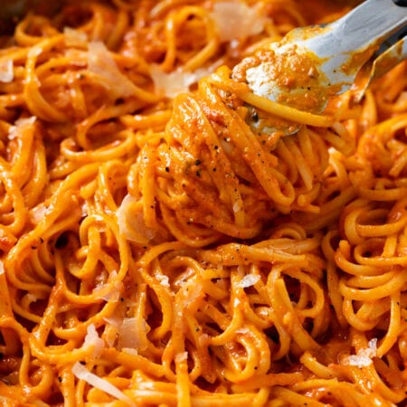 Kitchen Tongs lifting up Roasted Red Pepper Pasta from a skillet.