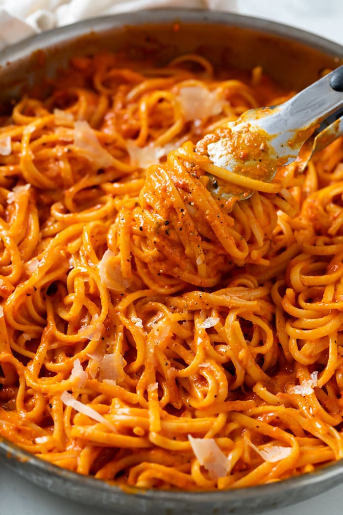 Kitchen Tongs lifting up Roasted Red Pepper Pasta from a skillet.