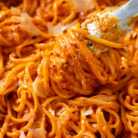 Roasted Red Pepper Pasta wrapped around kitchen tongs in a skillet.