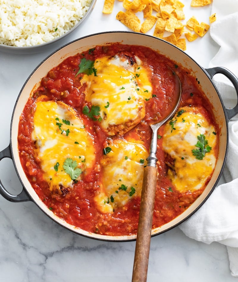 A skillet filled with Salsa Chicken topped with cheese and cilantro with a spoon in it.